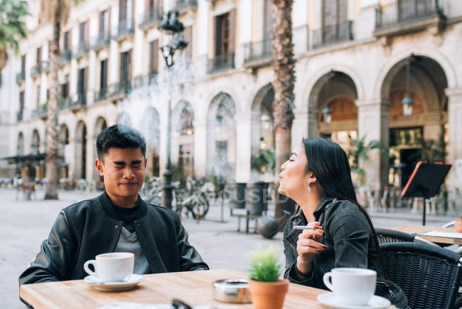 Mujer joven soplando humo de cigarrillo en la cara del novio - foto de stock