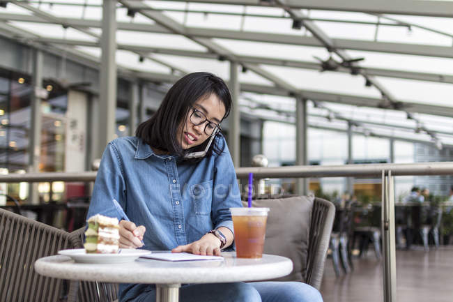 Jeune femme Jotting vers le bas quelques informations à un café . — Photo de stock