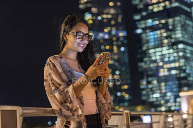 Молода жінка грає зі своїм смартфоном у місті — стокове фото