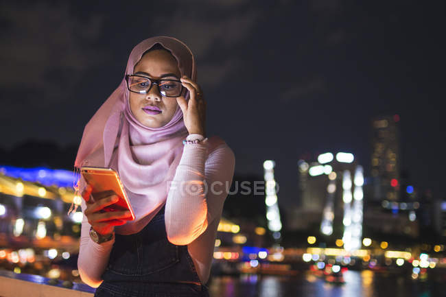 Jovencita usando su teléfono móvil en la calle, fondo de luz nocturna - foto de stock