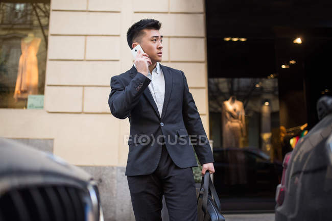 Chinese businessman talking on the phone in the street next to a luxury shop in Serrano Street, Madrid, Spain — Stock Photo