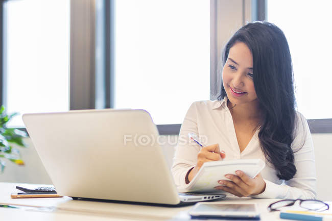Jovem mulher trabalhando por tomar notas no escritório moderno — Fotografia de Stock