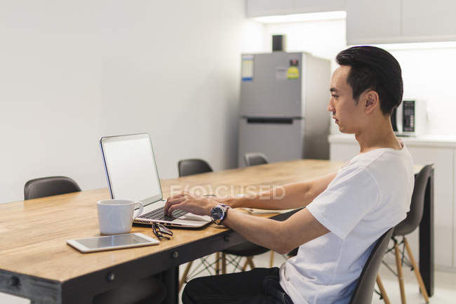 Hombre joven que trabaja con su ordenador portátil en el entorno de inicio - foto de stock