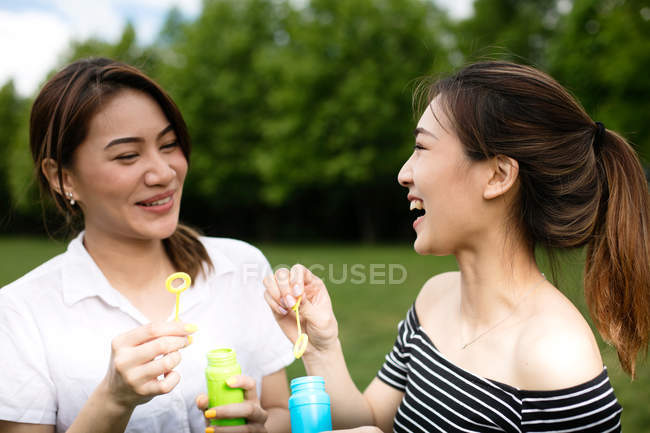 Niedliche asiatische Freundinnen machen Seifenblasen im Park. — Stockfoto