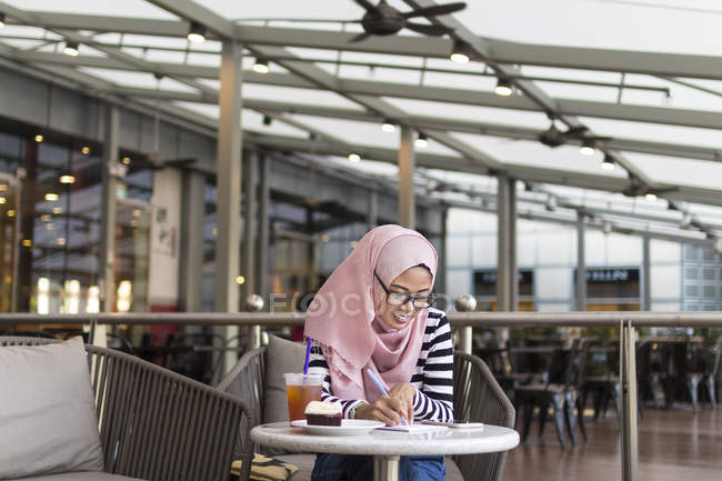 Jeune femme Jotting vers le bas quelques informations à un café — Photo de stock