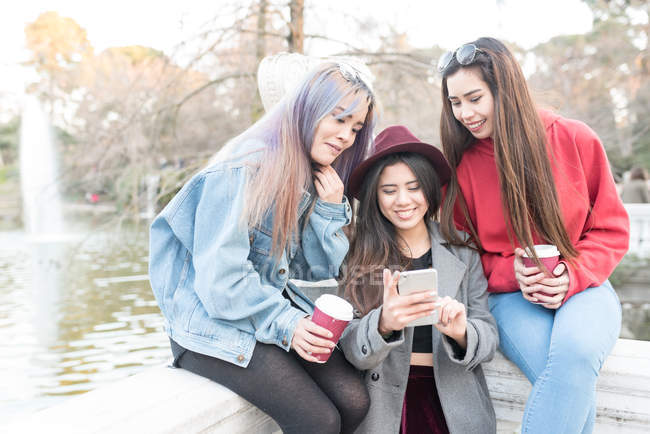 Amis naviguant sur le téléphone dans Retiro Park Madrid près du lac, Espagne — Photo de stock