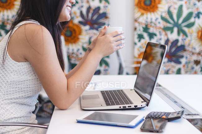 Mujer joven sosteniendo una taza de café en la oficina moderna - foto de stock