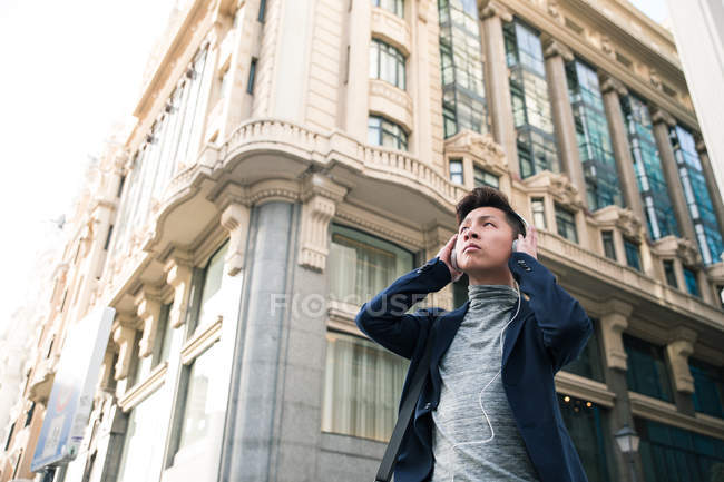 Lässiger junger chinesischer mann, der musik in gran via street, madrid, spanien hört — Stockfoto