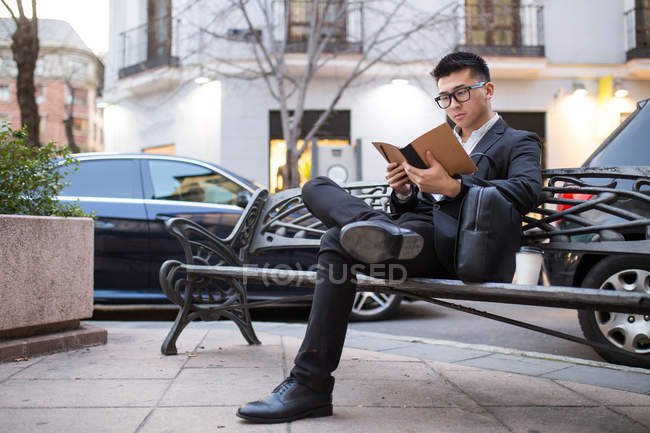 Chinese businessman reading in the street and sitting on a bench — Stock Photo