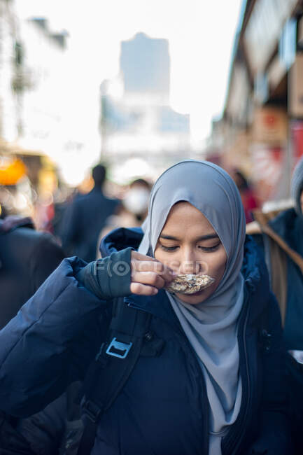 Retrato de mujer asiática incidental comiendo ostra en la calle - foto de stock