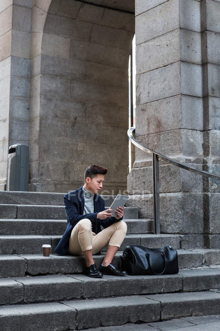 Casual jeune Chinois assis avec une tablette dans un escalier à Madrid, Espagne — Photo de stock