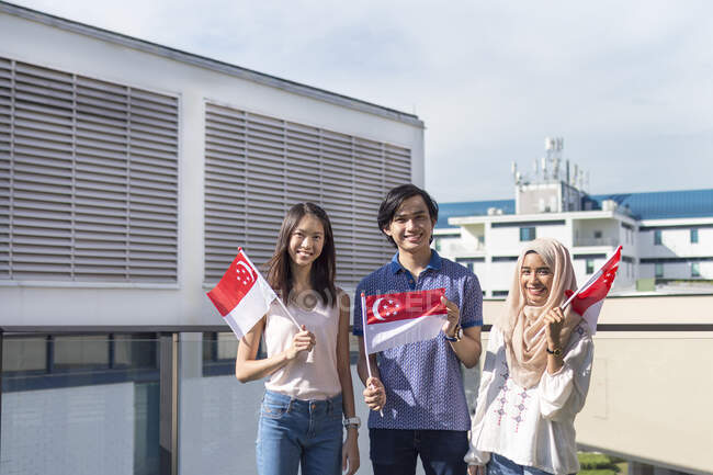 Un gruppo di amici in posa con le bandiere di Singapore. — Foto stock