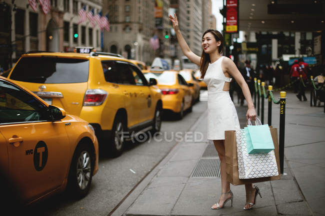 Молода жінка родом жовті таксі в місті після її великі покупки. — стокове фото