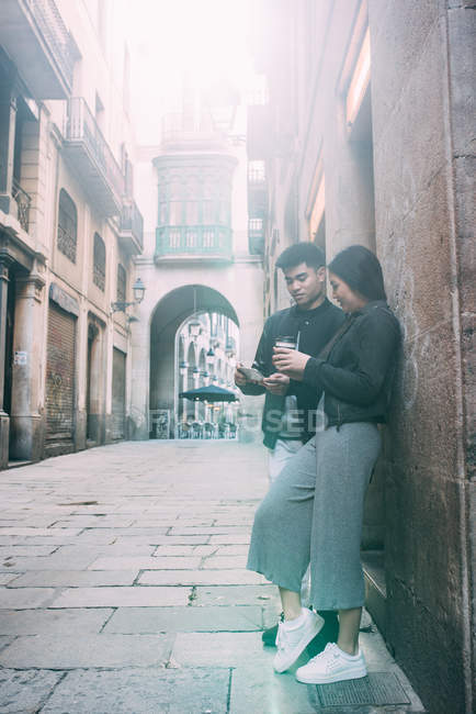 Young asian couple having coffee on the street and looking at the mobile phone — Stock Photo