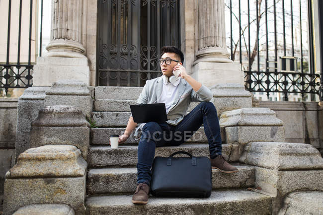 Homme d'affaires chinois parlant au téléphone et utilisant un ordinateur dans la rue, Espagne — Photo de stock