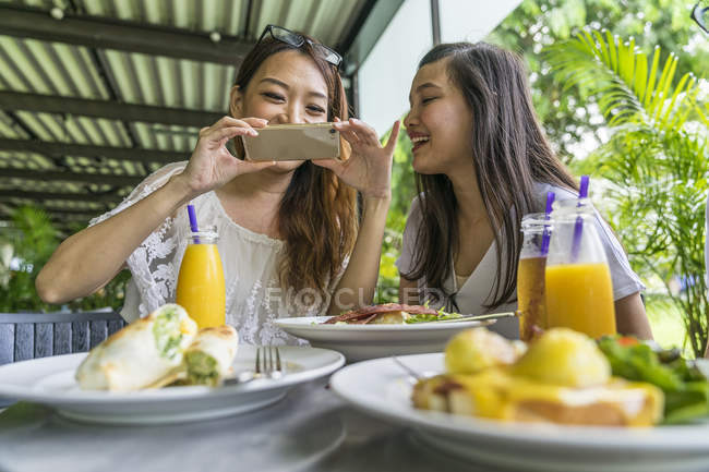Дівчина робить фотографії їжі в той час як її друг дивлячись на її телефон . — стокове фото