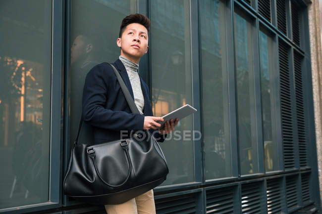 Casual jovem chinês olhando para longe segurando um computador tablet em Madrid, Espanha — Fotografia de Stock