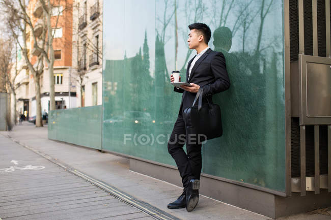 Китайский бизнесмен, стоящий на улице с чашкой кофе и планшетным компьютером, Испания — стоковое фото