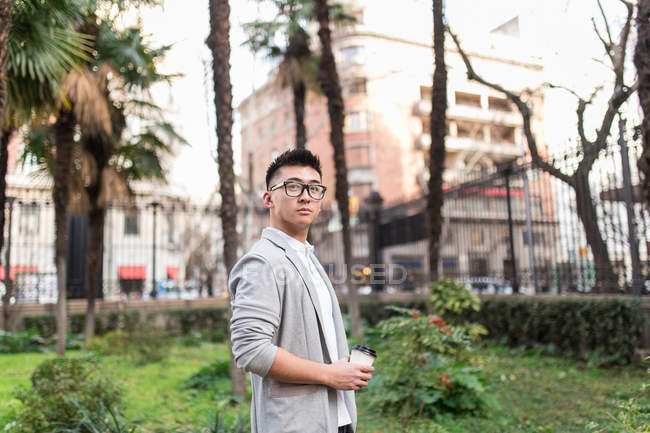 Hombre de negocios chino parado al aire libre sosteniendo una taza de café, España - foto de stock