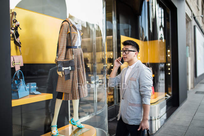 Китайский бизнесмен разговаривает по телефону на улице рядом с роскошным магазином на улице Серрано, Мадрид, Испания — стоковое фото