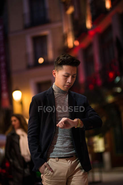 Lässiger junger chinesischer Mann, der nachts auf der Straße auf seine Uhr schaut, Spanien — Stockfoto