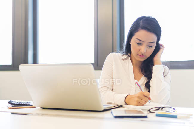 Joven mujer anotando notas en la oficina moderna - foto de stock
