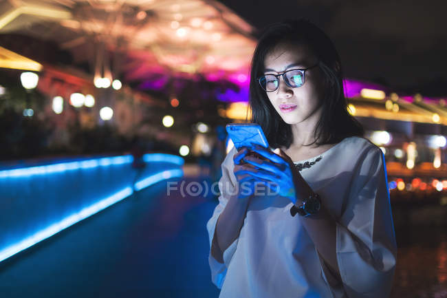 Молодий леді, використовуючи свій мобільний телефон на вулиці, ніч світлому фоні — стокове фото