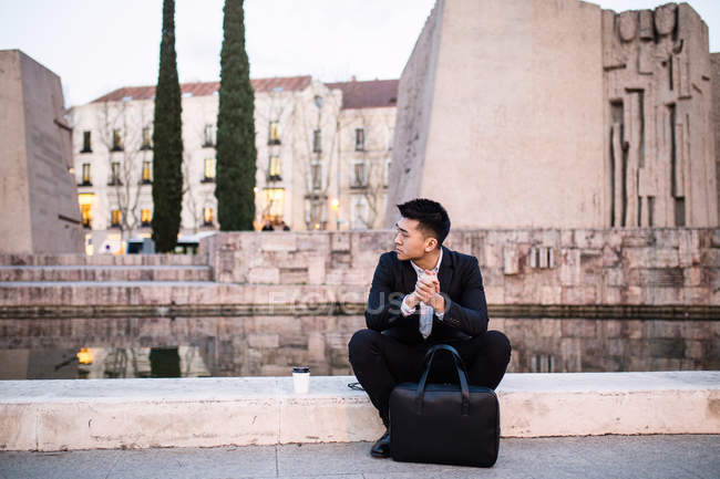 Pensativo empresario chino sentado en la calle pensando en nuevas ideas para los negocios, España - foto de stock