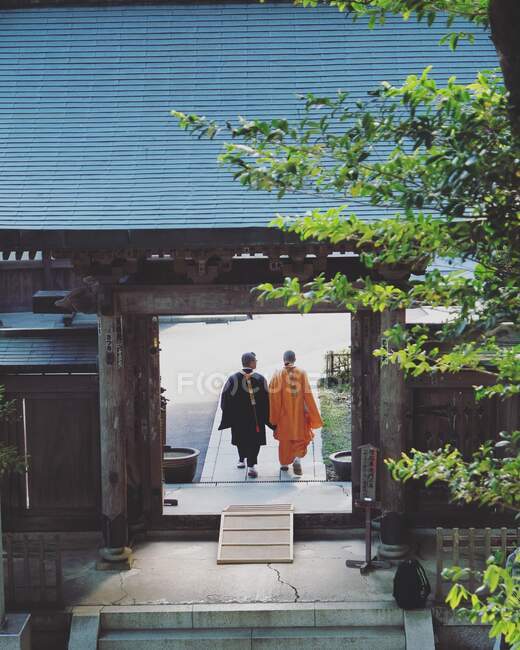 Dos monjes budistas pasan por una puerta en un templo en el monte Takao. - foto de stock