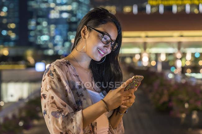 Молодая женщина играет со своим смартфоном в городе — стоковое фото