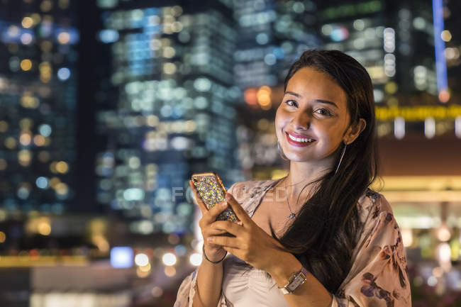 Молода жінка грає зі своїм смартфоном у місті — стокове фото