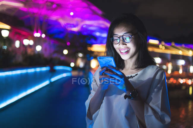 Junge Frau mit ihrem Handy auf der Straße, nachts Licht Hintergrund — Stockfoto
