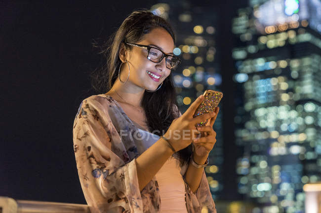 Mujer joven jugando con su teléfono inteligente en la ciudad urbana - foto de stock