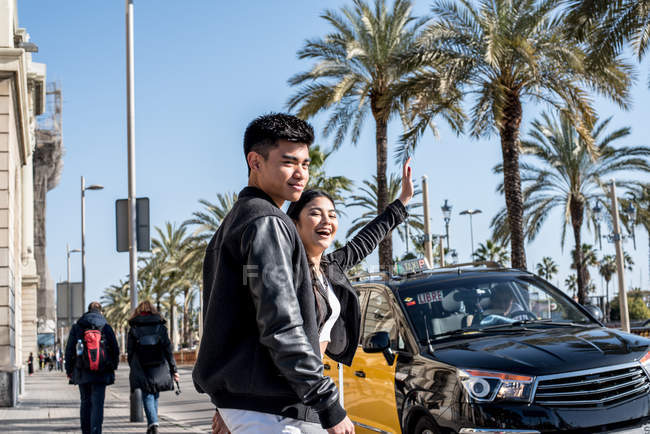 Pareja de turistas jóvenes agitando un taxi en la calle en barcelona, España - foto de stock