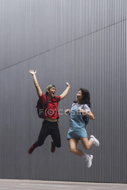 Jeunes étudiants asiatiques de collège sautant et posant contre le mur gris — Photo de stock