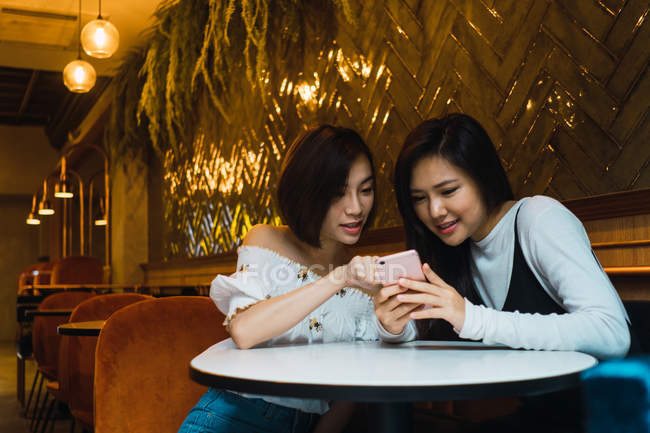 Jóvenes asiático mujeres amigos usando smartphone en cómodo bar - foto de stock