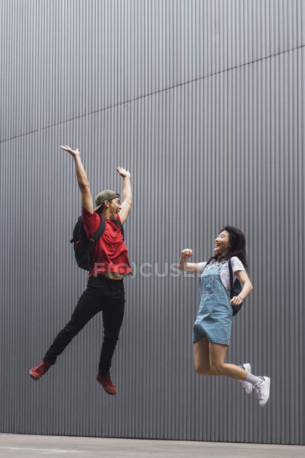 Jeunes étudiants asiatiques de collège sautant et posant contre le mur gris — Photo de stock