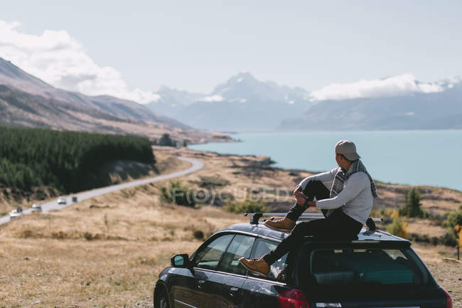 Rückansicht eines jungen Mannes, der auf einem Auto im Milford-Sound sitzt, Neuseeland — Stockfoto