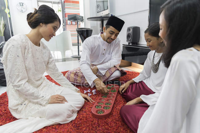 Felice famiglia asiatica che celebra hari raya a casa e giocare gioco tradizionale — Foto stock