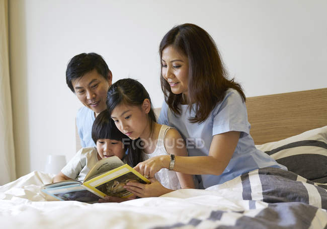 Familia compartiendo un libro en el dormitorio - foto de stock