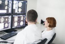 Dos doctores discutiendo imágenes de rayos X en pantallas de computadora - foto de stock