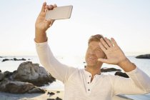 Uomo sorridente prendendo selfie sulla spiaggia — Foto stock