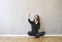 Женщина, сидящая на полу, делает селфи — стоковое фото
