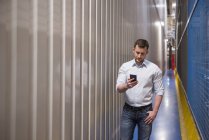 Un homme dans un couloir dans une usine regardant un téléphone portable — Photo de stock
