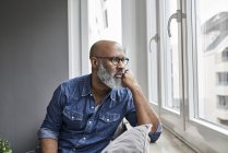 Mature man sitting at window, looking worried — Stock Photo