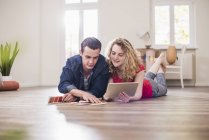 Young couple in new home lying on floor with tablet choosing from color sample — Stock Photo