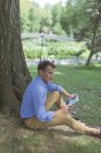 Mann mit Mini-Tablet sitzt im Park — Stockfoto