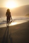 Silhouette einer Frau, die an einem Strand in den Sonnenuntergang geht, während sie ein Bikini-Oberteil trägt — Stockfoto