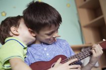 Хлопчик грає ukulele, а брат — стокове фото