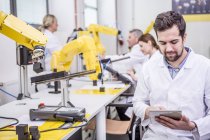 Ingeniero usando tableta en fábrica con robots industriales - foto de stock